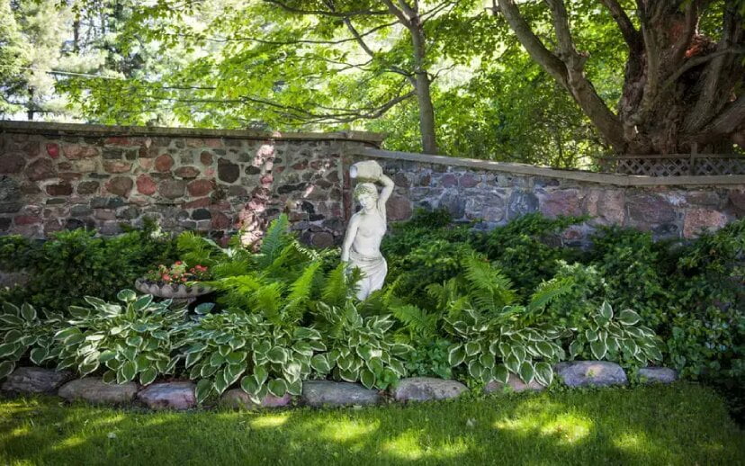 Plantes dans un jardin ombragé par un arbre le long d'un mur avec une statue au centre